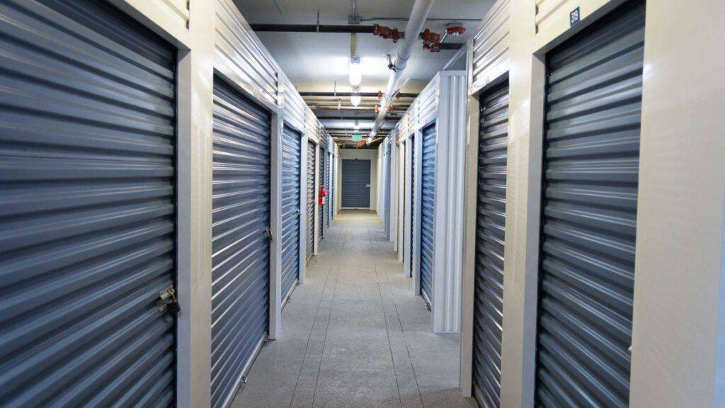 A clean, well-lit hallway of indoor storage units with blue doors
