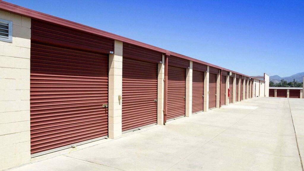 Row of outdoor storage units with large, red doors in a secure area