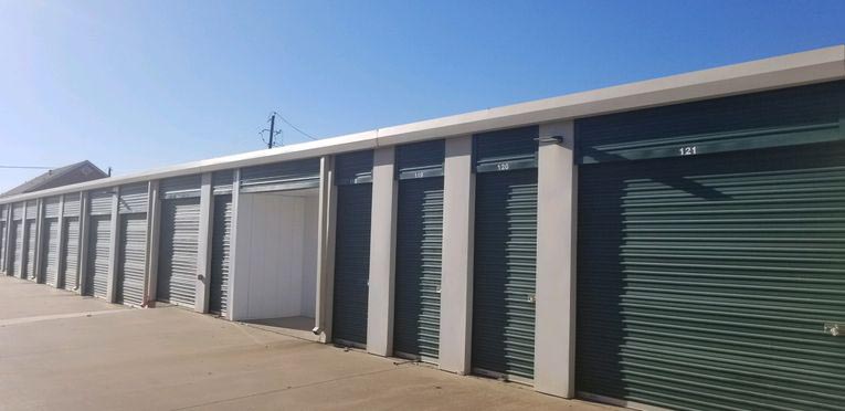 A row of small and large outdoor storage units with green doors