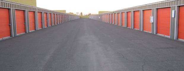 A long row of large outdoor storage units with orange doors in a clean area