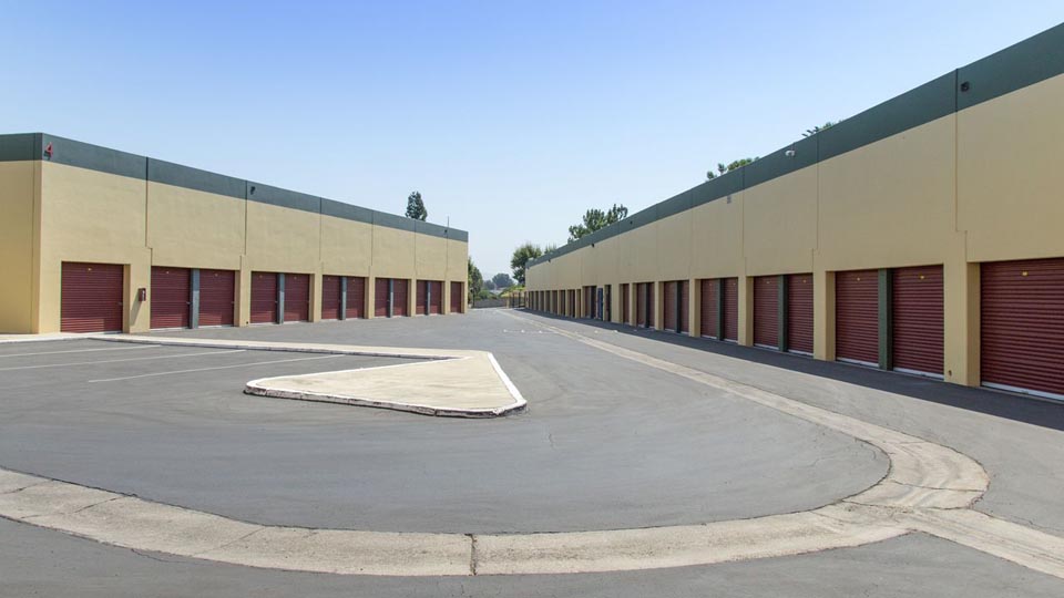An outdoor area of large storage units with parking and a long driveway