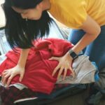 A woman trying to pack an overflowing suitcase of clothes