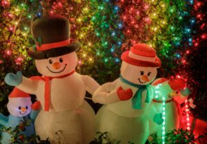An inflatable snowman family with rainbow lights at nighttime.